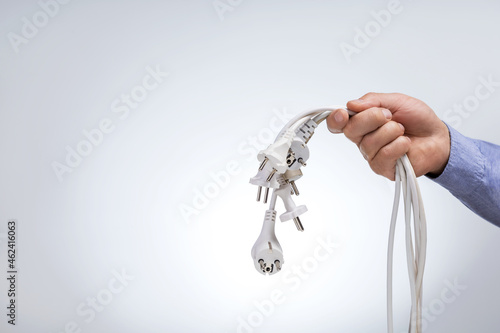 Fotografie Hand holding many electrical plugs on a grey background with copy space
