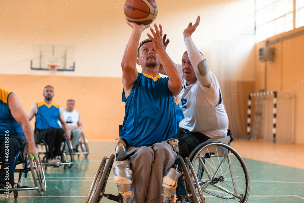 Disabled War veterans mixed race and age basketball teams in wheelchairs playing a training match in a sports gym hall. Handicapped people rehabilitation and inclusion concept - obrazy, fototapety, plakaty 