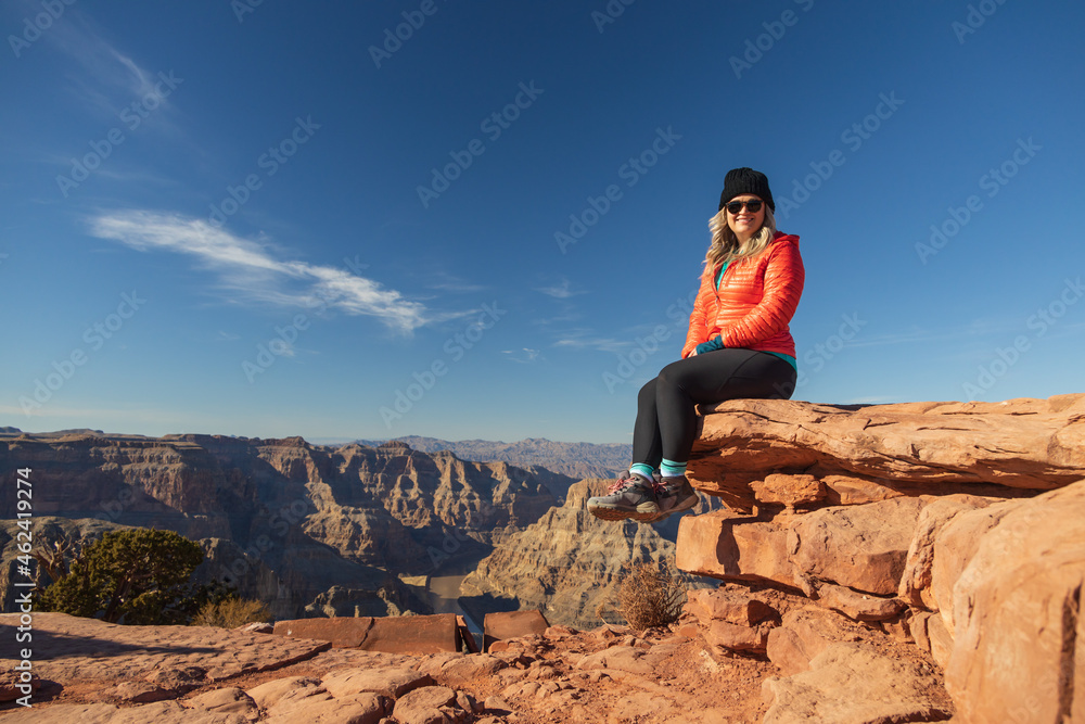Naklejka premium Smiling girl sitting on rock overlooking the Grand Canyon, Arizona, USA 