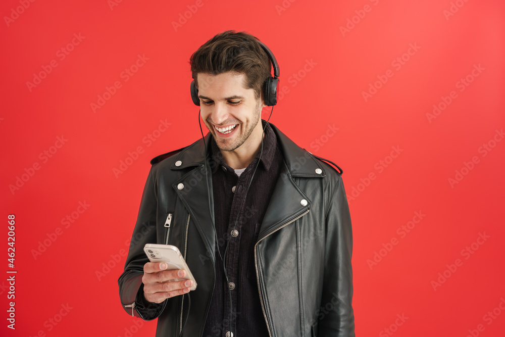Young unshaven man smiling while using cellphone and headphones Young unshaven man smiling while using cellphone and headphones