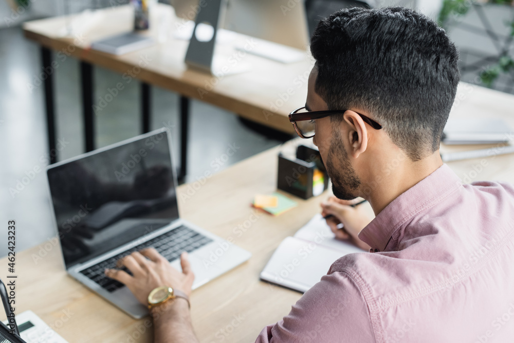 Arabian businessman in eyeglasses using blurred laptop in office Arabian businessman in eyeglasses using blurred laptop in office