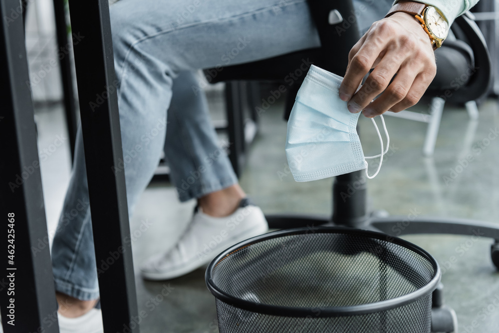 Cropped view of businessman holding medical mask near trash can in office Cropped view of businessman holding medical mask near trash can in office