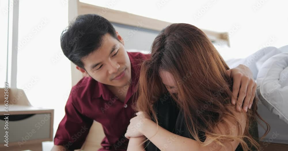 Loving Asian man trying reconcile with his wife after quarrel. Guy embracing his crying suppose while sitting at their bed room. Loving Asian man trying reconcile with his wife after quarrel. Guy embracing his crying suppose while sitting at their bed room.