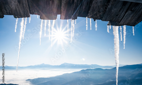 Spectacular icicles shine in sun against blue sky. Splendid view with ice icicles hanging from roof.