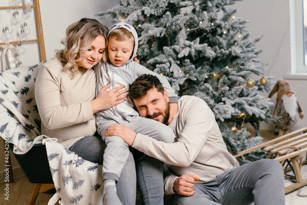 Christmas Family Happiness Portrait of dad, pregnant mom and little son  sitting armchair at home near Christmas tree hug smile