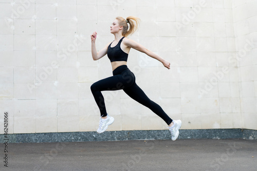 Sport and Fitness Concept Young Adult Caucasian Female Athlete Jumping High Outdoor Gray Tail Wall Background