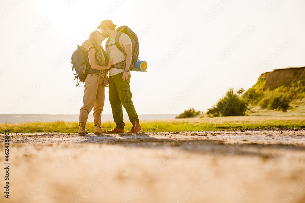 White couple with backpacks kissing while hiking together outdoors