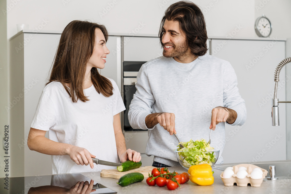 Young multiracial couple talking while making salad together Young multiracial couple talking while making salad together