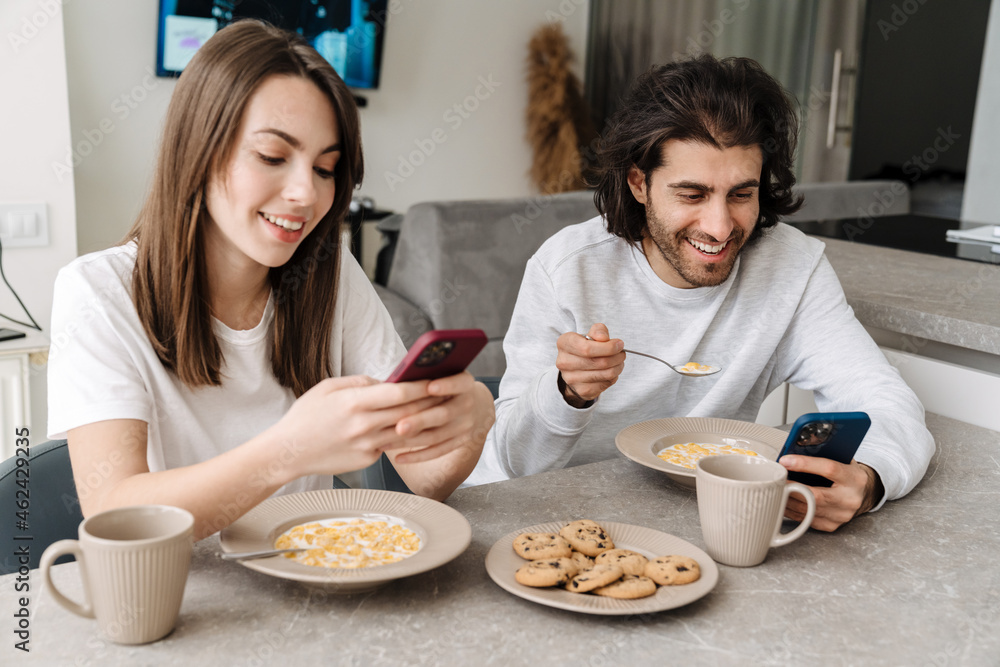 Young multiracial couple using cellphones while having breakfast Young multiracial couple using cellphones while having breakfast