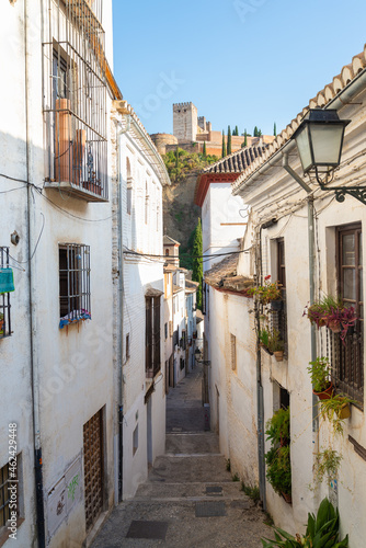 The neighborhood named  Albaicin  in Granada  Andalusia  Spain. Narrow street with white ancient buildings at both sides. Alhambra hill visible in the distance.