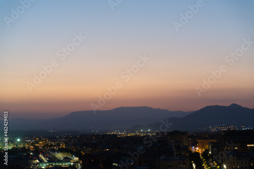 Aerial view of Granada, Andalusia, Spain at night. Urban city light in the foreground. Sierra Nevada mountain range with colorful sunset sky on the background. © Travelling Jack