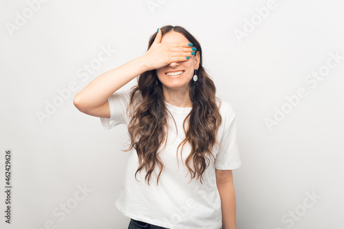 Happy smiling woman is covering her eyes with a hand.