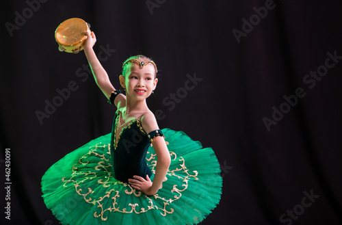 A little girl ballerina is dancing on stage in a tutu on pointe shoes with a tambourine, a classic variation of Esmeralda.