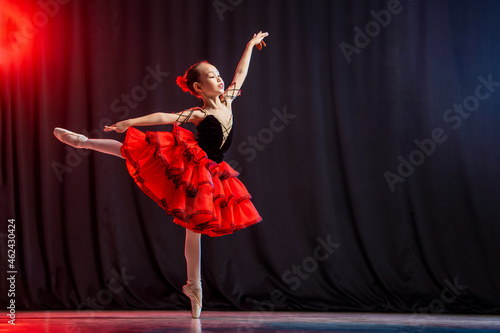 A little girl ballerina is dancing on stage in a tutu on pointe shoes with castanedas, the classic variation of Kitri. photo