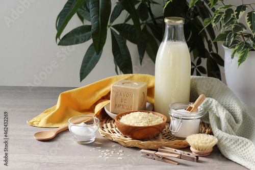 Foto Marseille soap bar, pure soap flakes, bicarbonate of soda, cotton towel, spoon, clothes peg, potted plant and home made laundry detergent in the glass bottle on the grey table