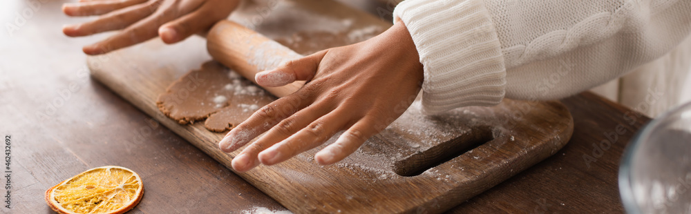 Cropped view of african american woman rolling dough near dry orange slice in kitchen, banner