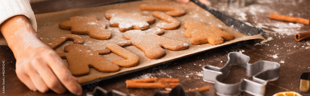 Cropped view of african american woman with hand in flour holding tray with christmas cookies and cinnamon, banner Cropped view of african american woman with hand in flour holding tray with christmas cookies and cinnamon, banner
