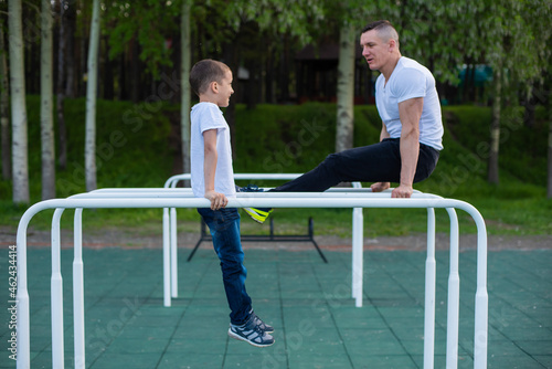 Caucasian man trains a boy on the uneven bars on the playground. Dad and son go in for outdoor sports.