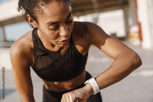 Black sportswoman looking at smartwatch while working out on parking