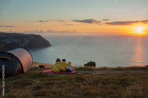 Beautiful family, camping on a hill, enjoying the sunset view on a summer day