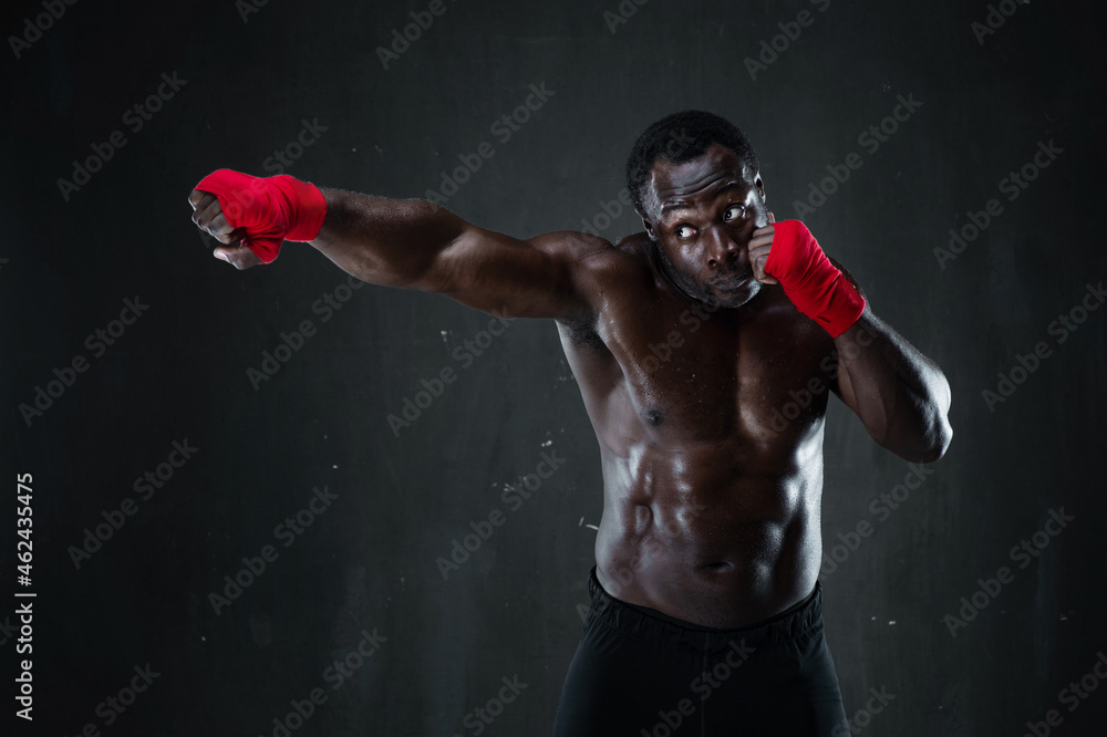 Athletic afro boxer during boxing training. Fitness african american muscular model over black background. Strength, fighting and motion project.