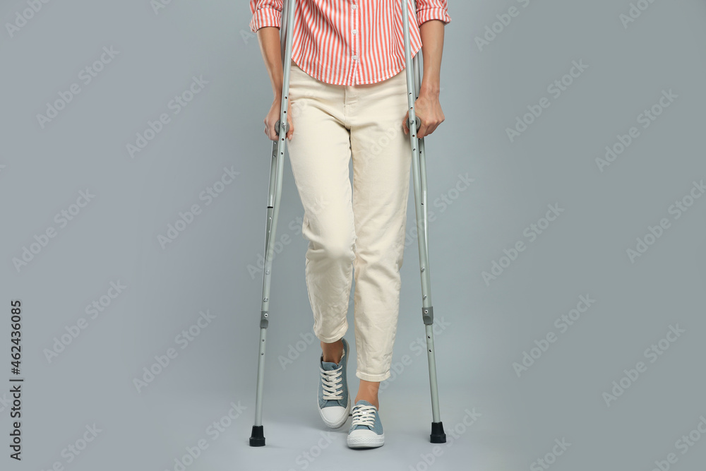 Young woman with axillary crutches on grey background, closeup Young woman with axillary crutches on grey background, closeup