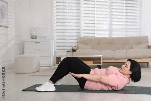 Overweight mature woman doing abs exercise at home, space for text