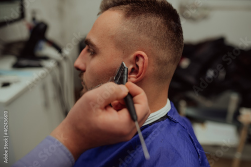The barber paints the beard and the mustache of the young man in the barbershop.Selective focus