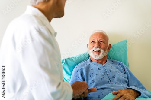 Obraz na płótnie Doctor talking to senior male patient in hospital bed who is recovering from the