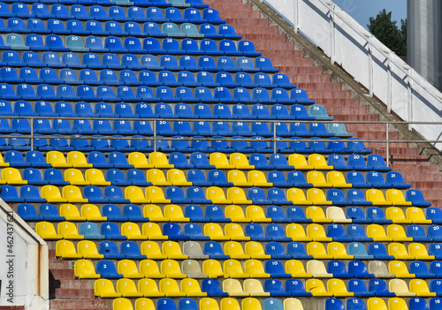 Tribune of fans at the stadium. Lots of rows with blue and yellow seats for people on the football field