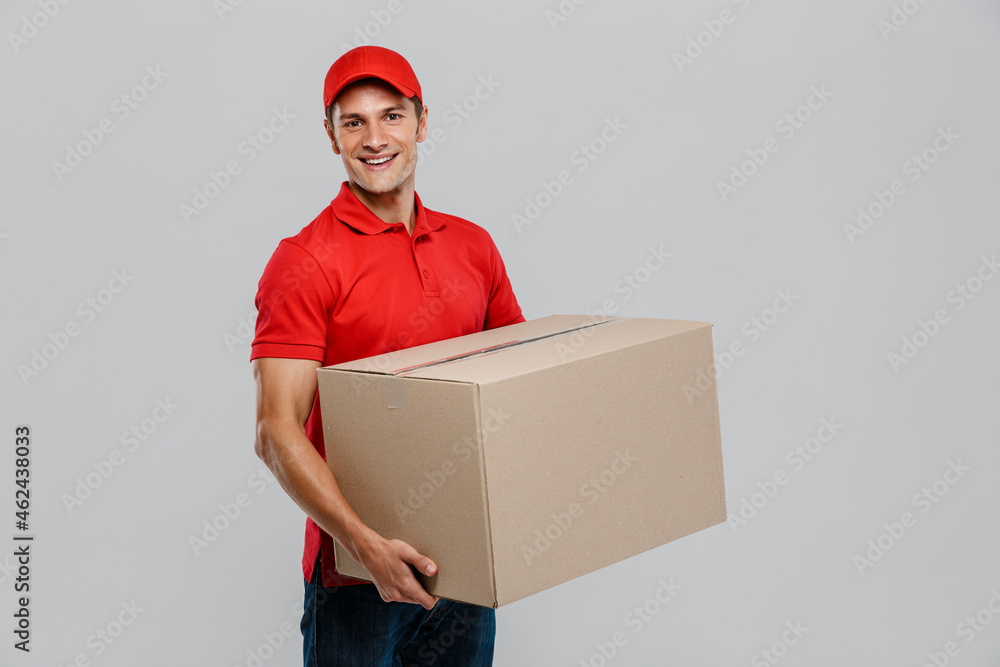 Young delivery man in hat smiling while posing with cardboard box Young delivery man in hat smiling while posing with cardboard box
