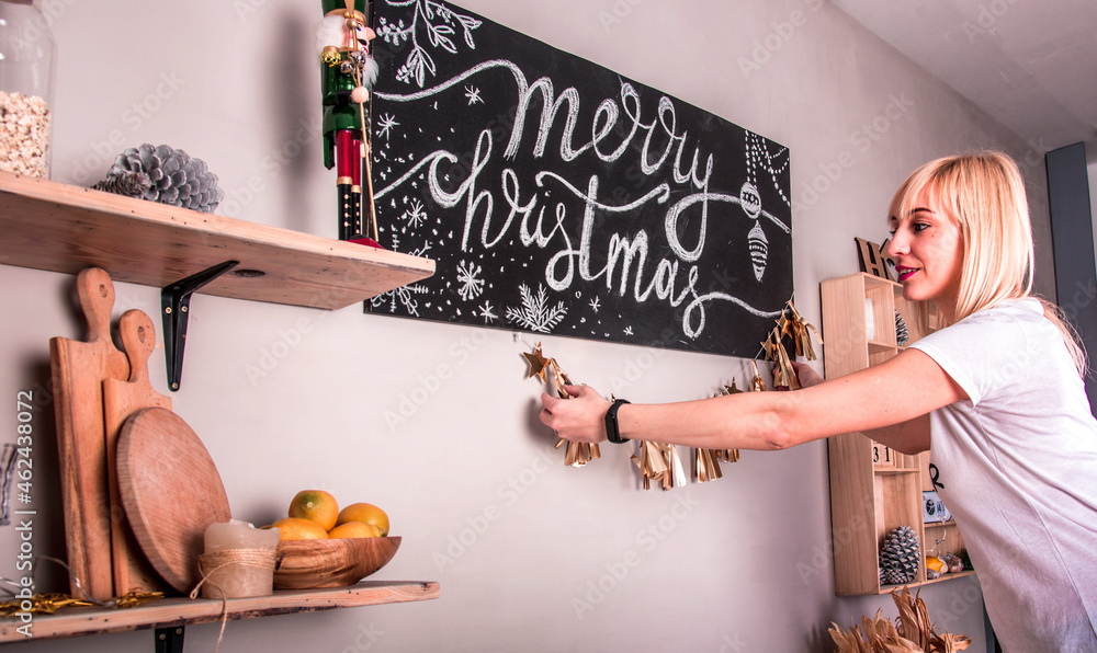 Beautiful smiling young girl hangs glitter decorations around poster with Merry Christmas inscription