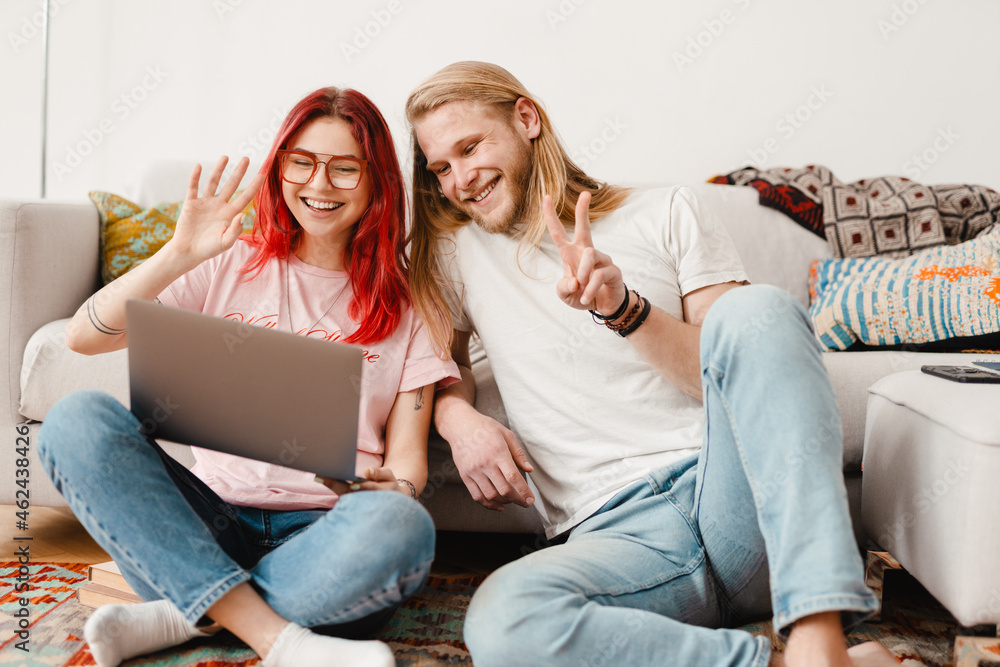 White man and woman gesturing and using laptop while sitting on floor White man and woman gesturing and using laptop while sitting on floor