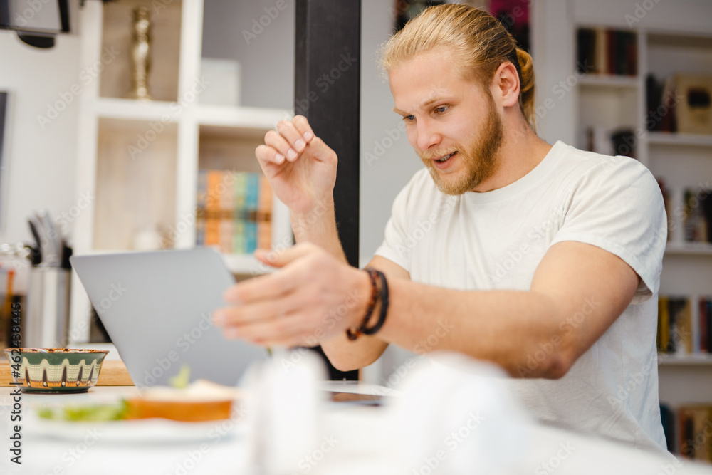 Bearded blonde man working with laptop while sitting on table Bearded blonde man working with laptop while sitting on table
