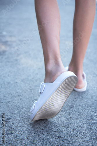 Female legs in white flip flops side view. Beautiful slender legs on the asphalt. Feet outside