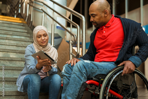 Muslim woman and disabled man using tablet computer together