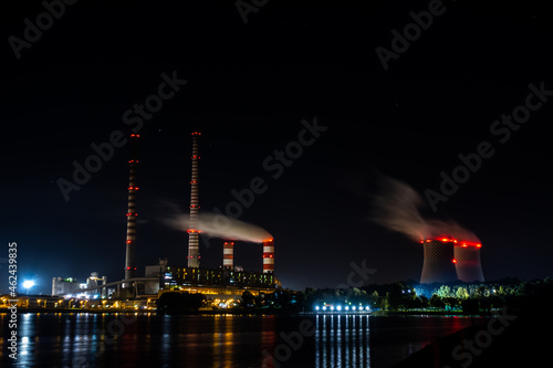 Night picture of distant black coal-fired power plant. Blurry view for the smoke coming out of the chimneys. Photo taken in evening under natural lighting conditions.