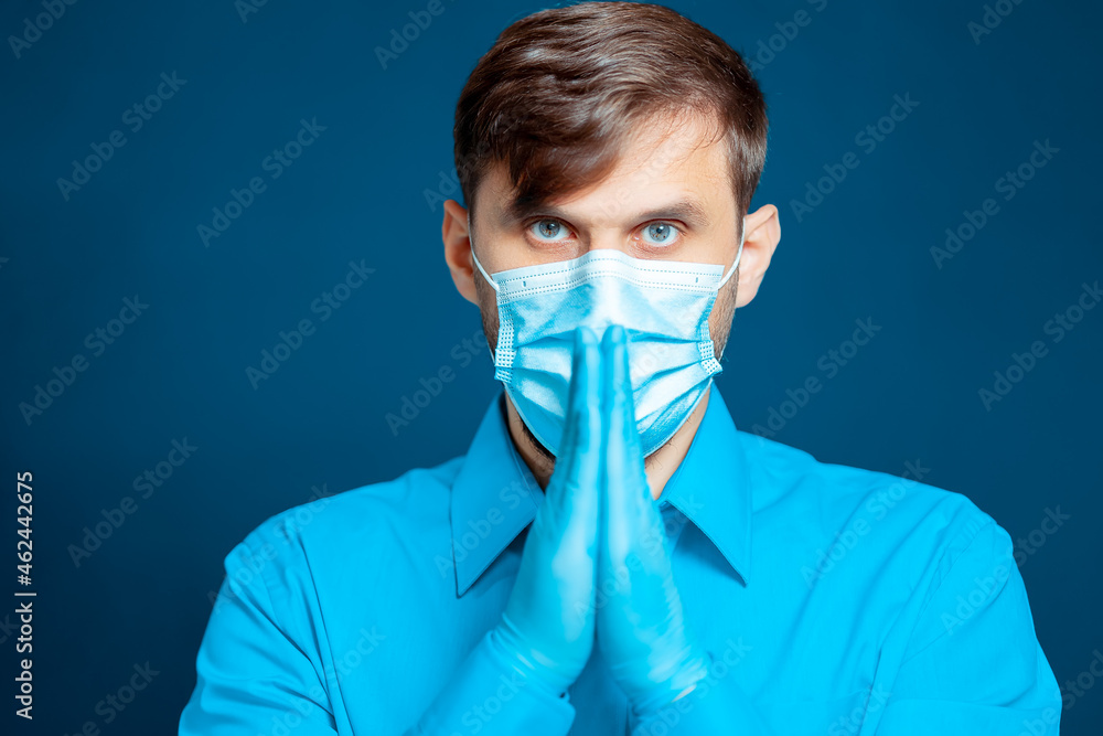 doctor in a medical mask and gloves, in a blue uniform gestures with his hands.