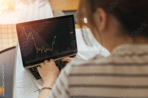 Young adult Asian trader, investor, businesswoman using computer laptop with graph chart in business money investing, stock market, Bitcoin Cryptocurrency trading at home. Financial investment concept