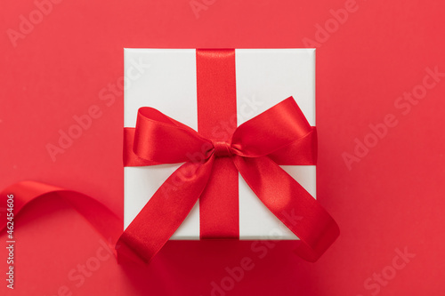 Gift box red ribbon and bow on red background, Christmas present satin curly decoration, © Rawf8