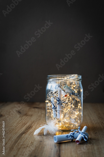 Ein Einmachglas mit Wunschzetteln und einer Lichterkette auf einem Holz Tisch. Schwarzer Hintergrund, leuchtend, Weihnachten. photo