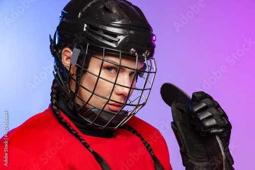 Photography Close-up portrait of woman, professional hockey player in helmet with stick isolated over gradient blue purple background