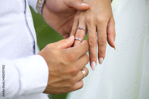 At the wedding ceremony, the groom puts a diamond engagement ring on the bride's finger, top view. Hands of newlyweds with rings close-up. Traditional wedding ceremony with putting on gold rings