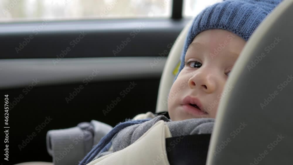 Winter road trip. A child in a winter jacket and hat travels in a car seat in the back seat of a car. The child is securely fastened with a seat belt. Safety of transportation of children. Close-up Winter road trip. A child in a winter jacket and hat travels in a car seat in the back seat of a car. The child is securely fastened with a seat belt. Safety of transportation of children. Close-up