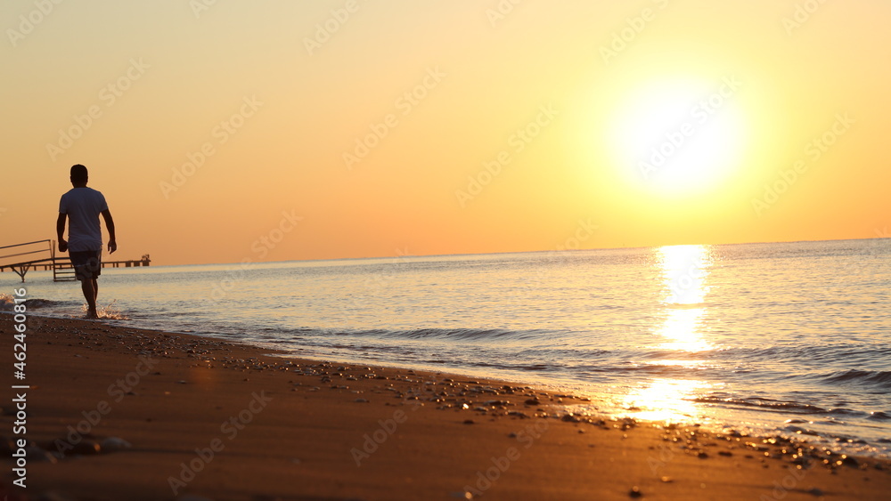 Young man walking on the beach at sunset