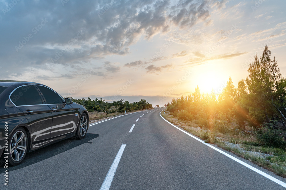 Black car on a scenic road. Car on the road surrounded by a magnificent natural landscape in the rays of sunset or dawn. Black car on a scenic road. Car on the road surrounded by a magnificent natural landscape in the rays of sunset or dawn.