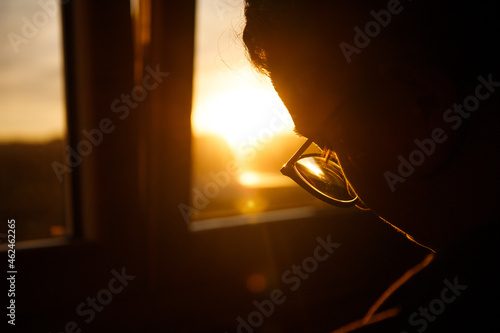 very closeup side view of silhouette from a young woman with glasses working indoors during sunset