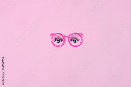 Creative makeup concept with  pink glasses, eyelashes and orchid flowers on the pink background. Makeup concept.