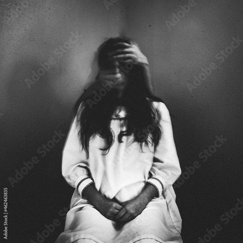 Creepy ghost girl sitting in chair with eerie hands grabbing her face