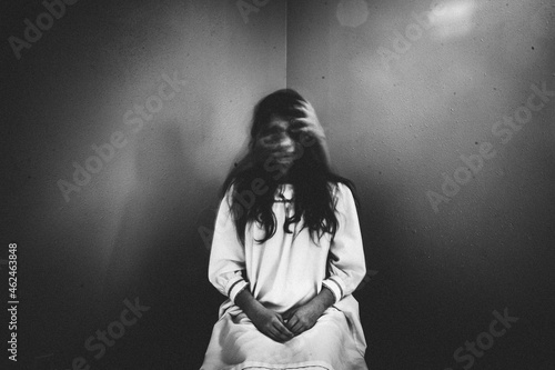 Creepy girl sits in chair with ghostly hands covering her face photo